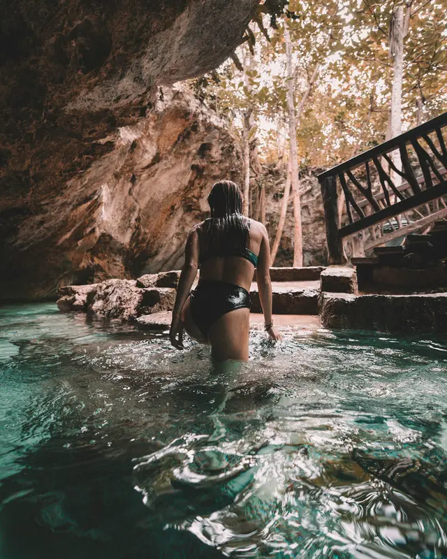 Woman stepping into a cavern cenote in Tulum